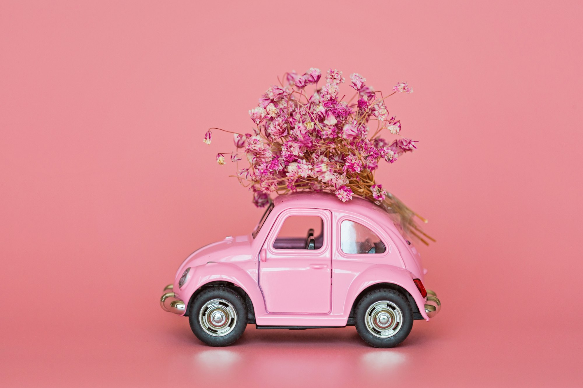 Mockup for delivery services with toy car and bouquet of flowers on roof on pink background